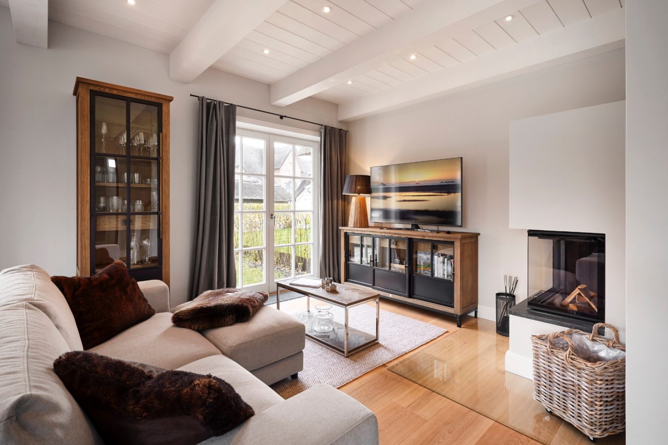 Moderner Wohnraum mit hellen Wänden, Sofa, TV und Kamin. Große Fenster mit Vorhängen.