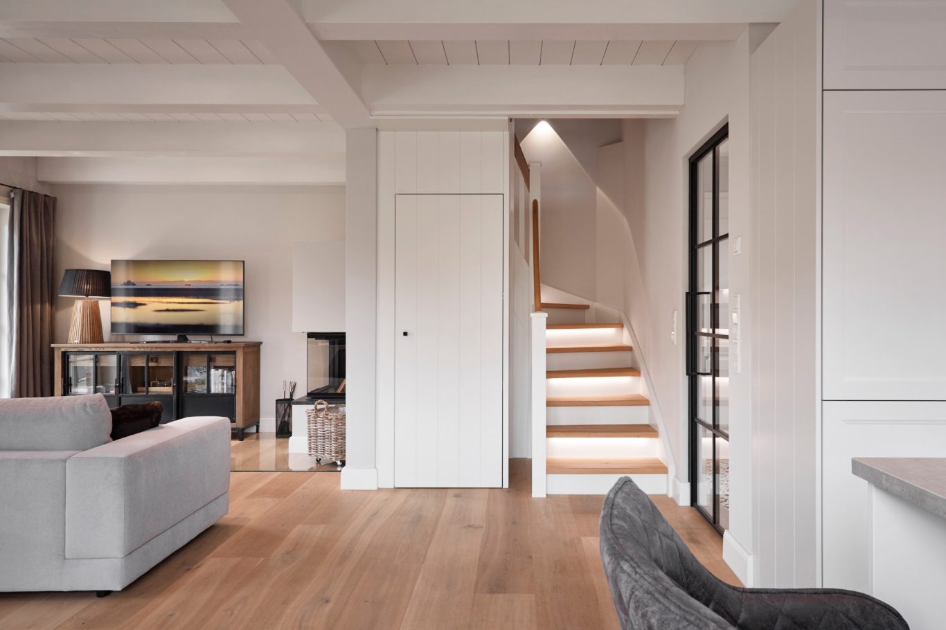 Helles Wohnzimmer mit Sofa, Fernseher und Treppe im Hintergrund. Minimalistischer Stil.