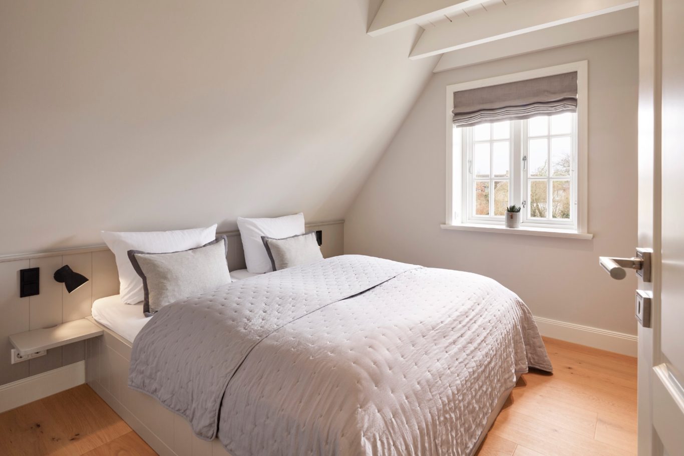 Helles Schlafzimmer mit Doppelbett, grauen Wänden und Fenster mit Rollläden.