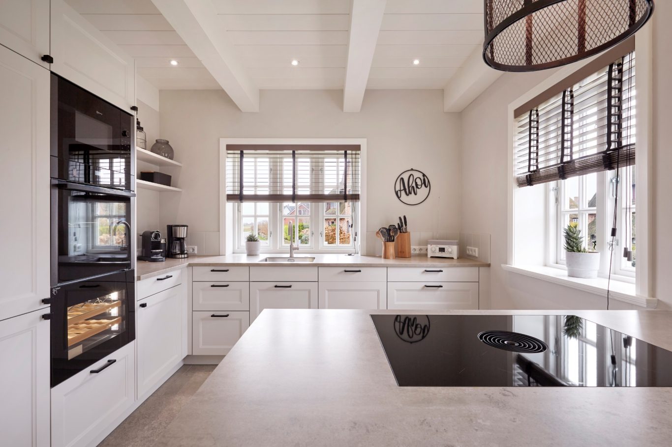 Moderne Küche mit Kochinsel, hellen Möbeln und großen Fenstern.