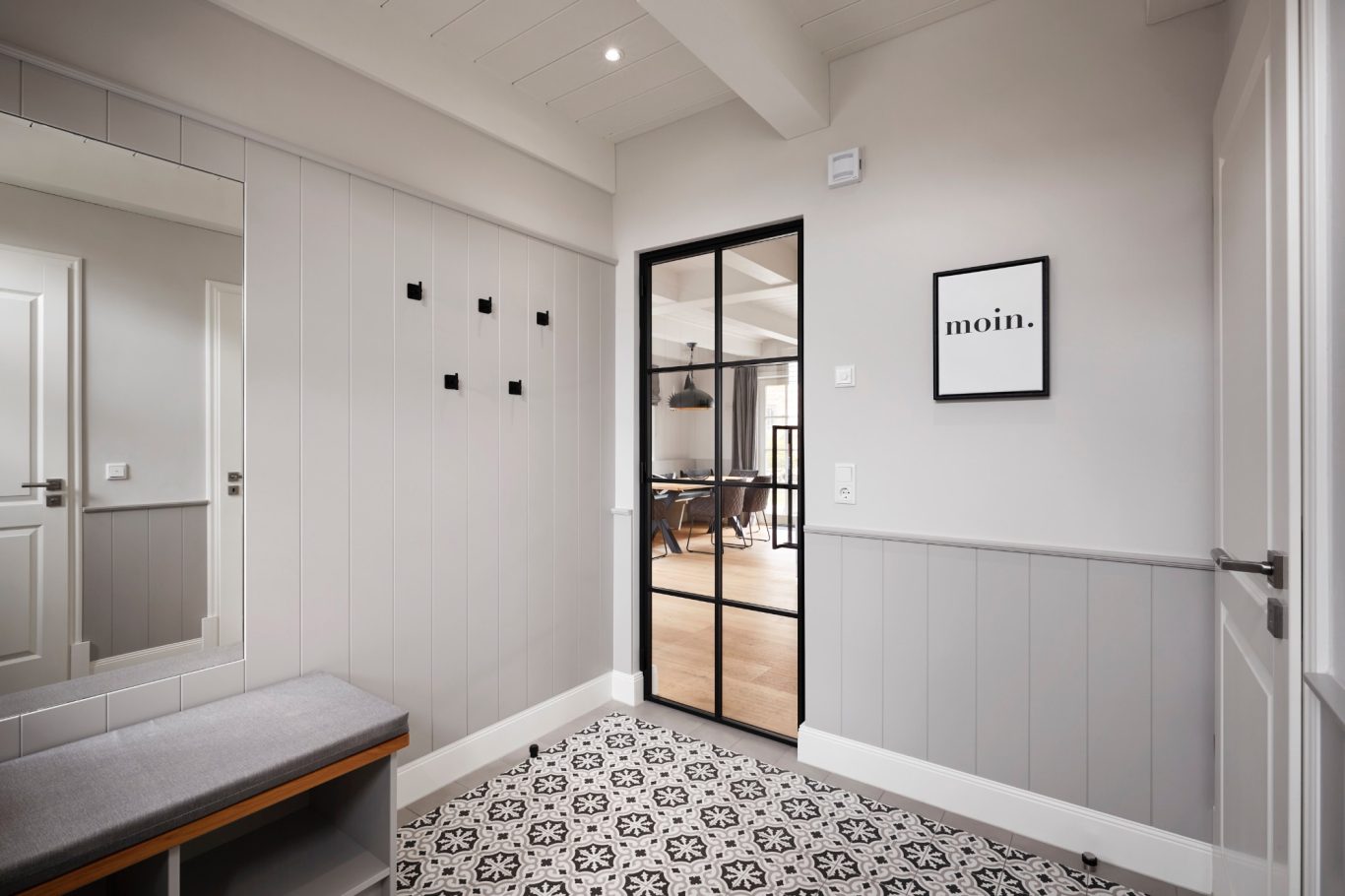 Heller Eingangsbereich mit grauen Wänden, Fliesenboden und einer Glastür.