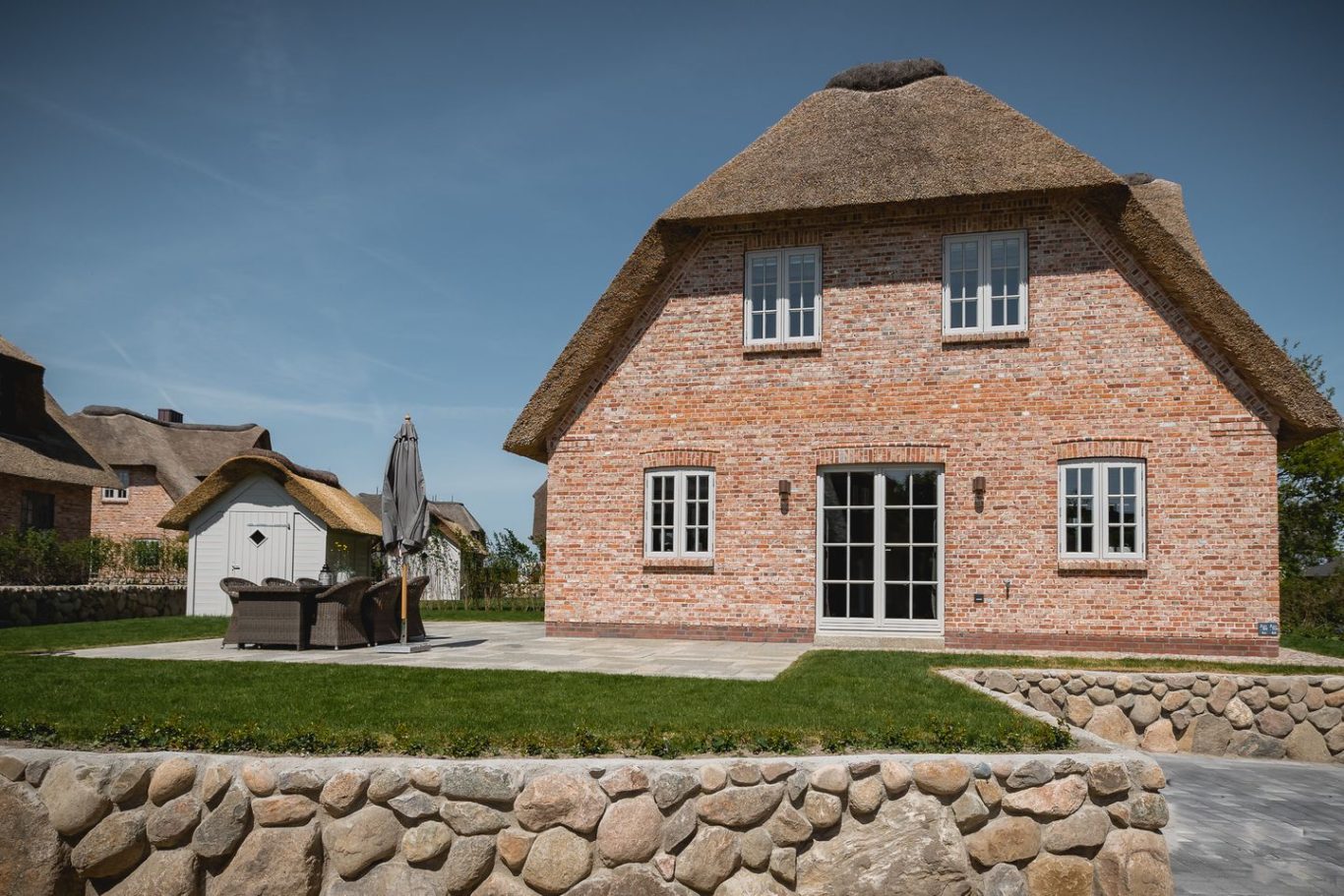 Ferienhaus mit Reetdach und Terrasse in ländlicher Umgebung.