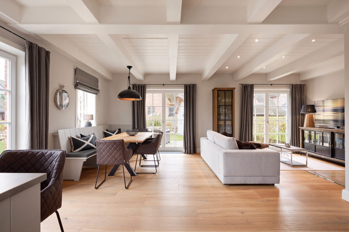 Helles Wohnzimmer mit Holzboden, großen Fenstern und moderner Einrichtung.