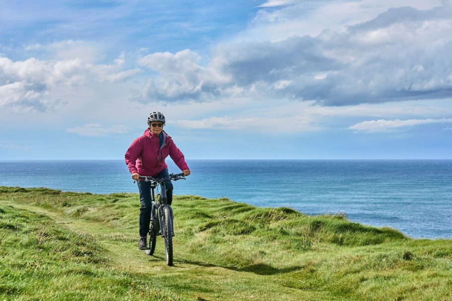 Radfahrer fährt auf einem Weg entlang der Küste mit Meerblick und bewölktem Himmel.