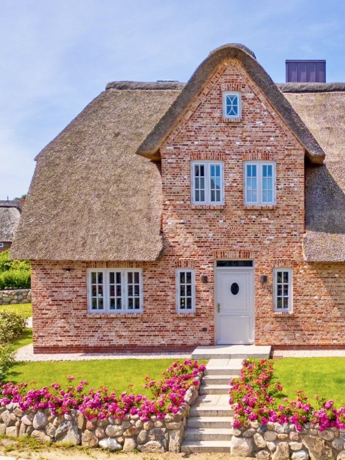 Traditionelles, Ferienhaus mit Reetdach und bunten Blumen im Vorgarten.