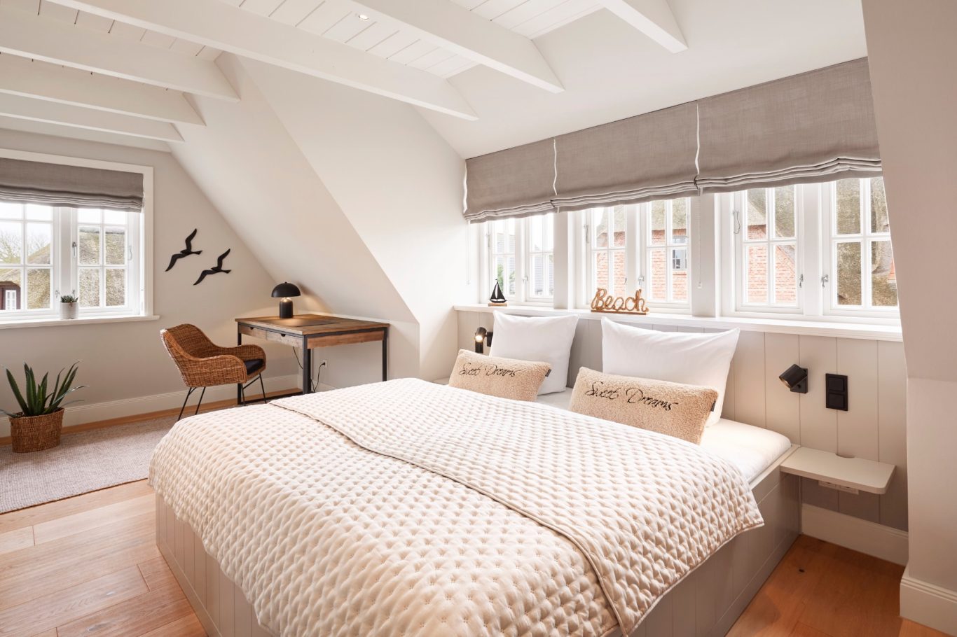 Helles, minimalistisches Schlafzimmer mit Doppelbett und Schreibtisch unter schrägen Wänden.