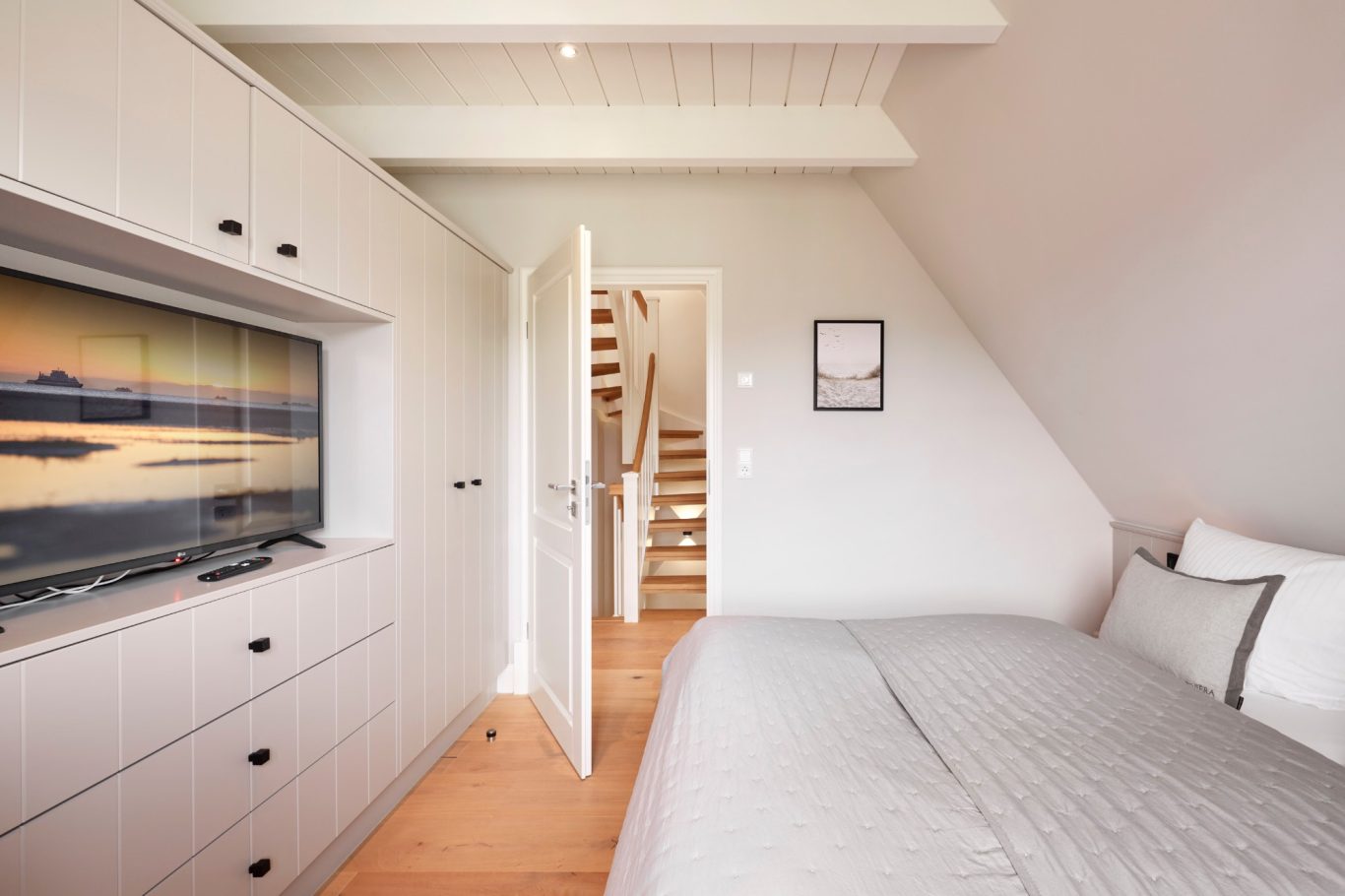 Helle Schlafzimmer mit Bett, Fernsehschrank und offener Tür zu den Treppen.